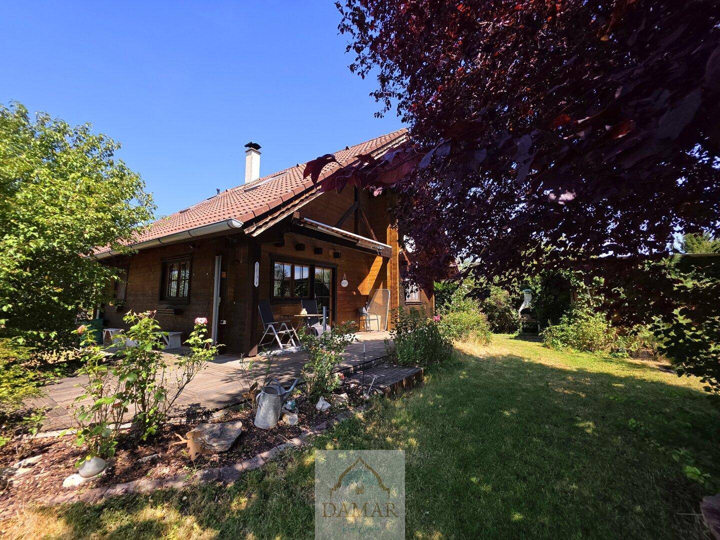 Charmantes Holzhaus mit sonniger Terrasse und gepflegtem Gartenbereich unter blauem Himmel.