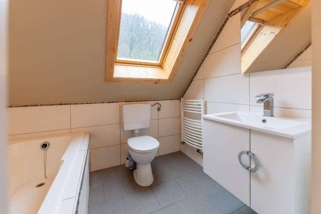Modernes Badezimmer im Dachgeschoss mit Badewanne, WC, Waschbecken und einem Dachfenster.