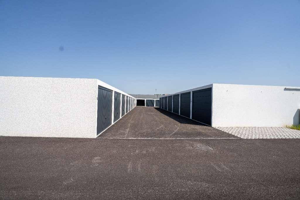 Reihen moderner Garagenboxen mit dunklen Toren und einer asphaltierten Zufahrt unter blauem Himmel.