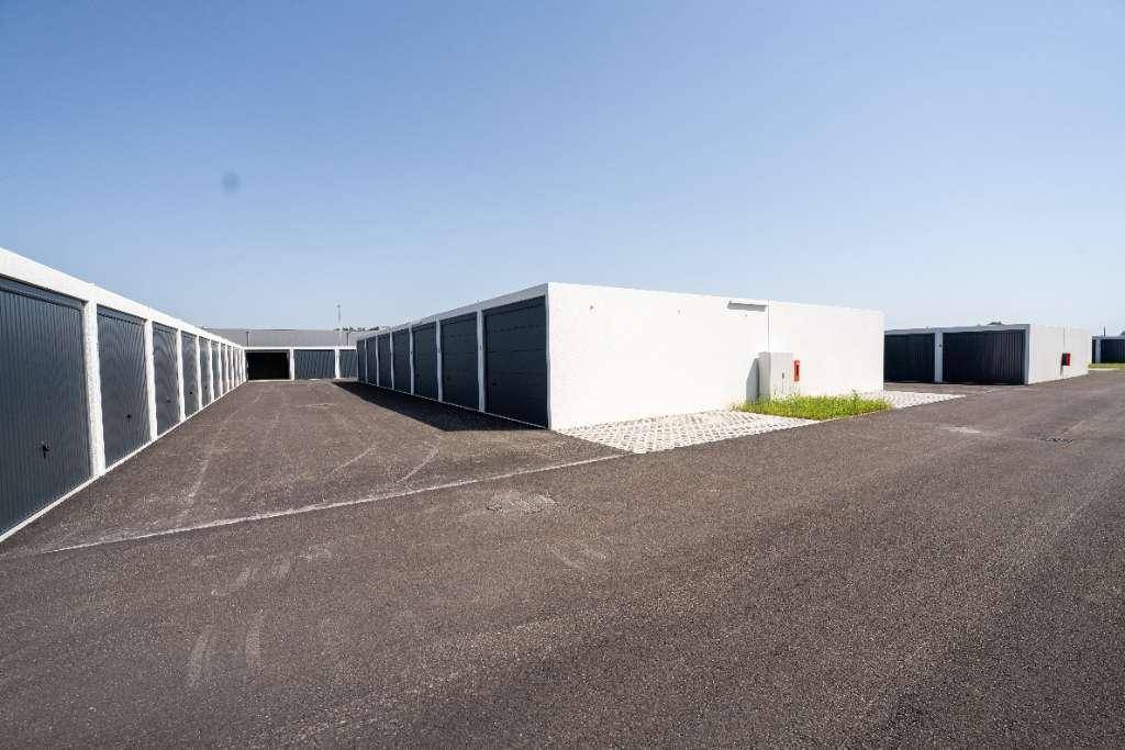 Lange Reihen moderner Garagenboxen mit dunklen Toren und asphaltierter Zufahrt unter klarem Himmel.