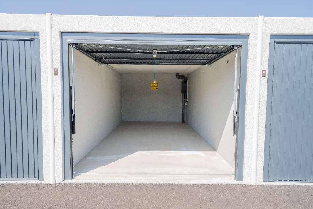 Leere und makellose Garagenbox mit offenem Rolltor, glattem Betonboden und hoher Decke.