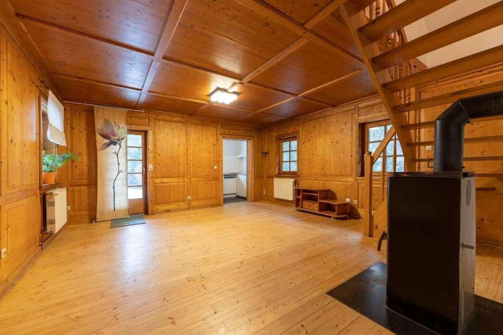 Gemütliches Wohnzimmer mit Holztäfelung, Holztreppe und einem traditionellen Kaminofen.