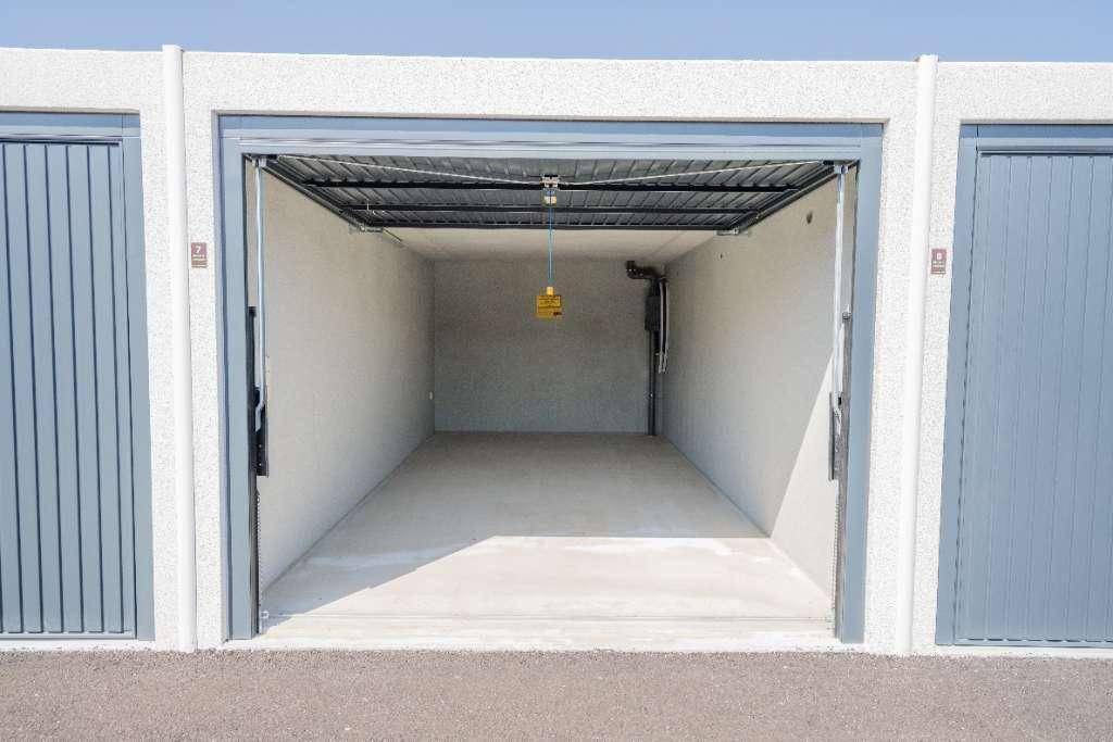 Leere Garagenbox mit offenem Tor, Betonboden und sauber gestrichenen Wänden.