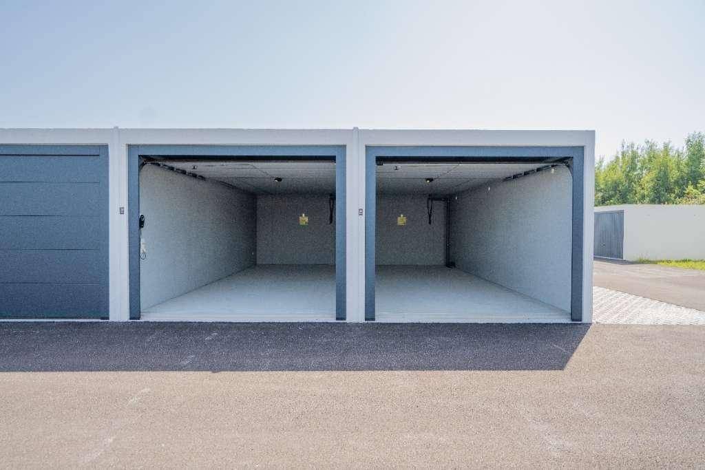 Zwei offene, leere Garagenboxen mit hellgrauen Wänden und dunklen Rolltoren, die auf ihre Nutzung warten.