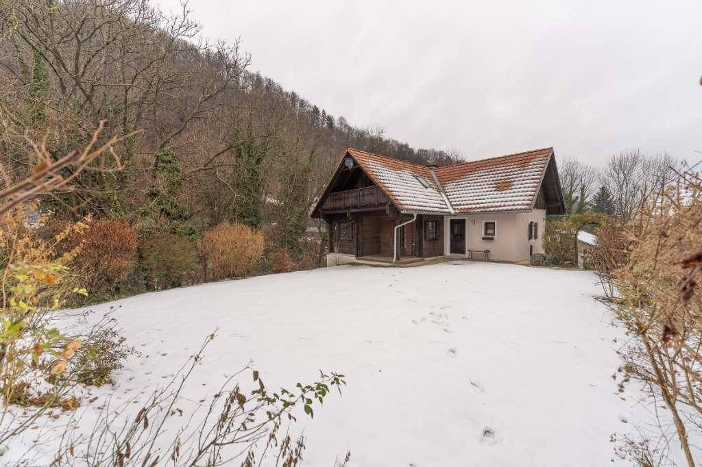 Freistehendes Haus mit rotem Ziegeldach in einer verschneiten Landschaft mit Hügeln im Hintergrund.