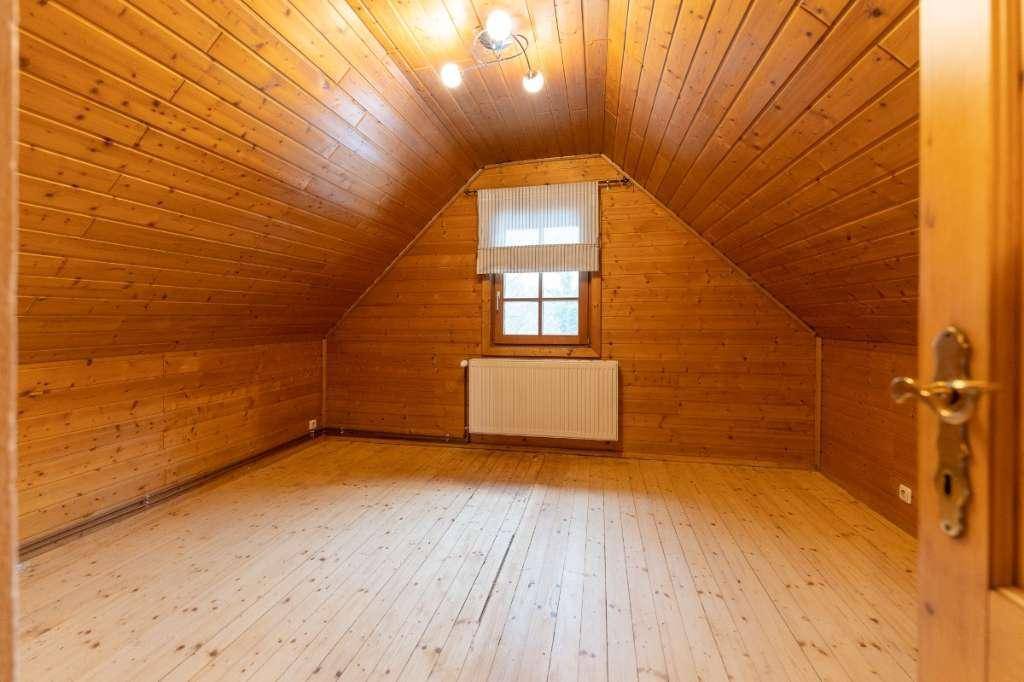 Dachgeschosszimmer mit Holzvertäfelung, schrägen Wänden und einem Fenster, ideal als Schlafzimmer.