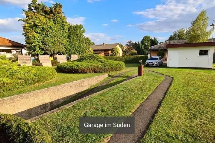 Großer Gartenbereich mit Zufahrt, Rasen und separater Garage unter blauem Himmel.
