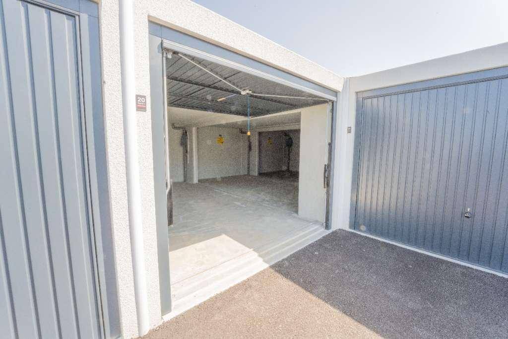 Offene Garagentür eines modernen Garagenkomplexes mit Blick in den leeren Innenraum und asphaltierter Zufahrt.