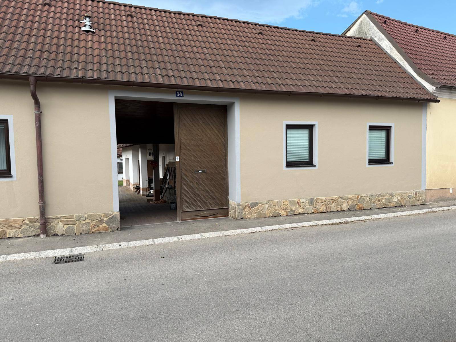 Hausfassade mit großem Holztor, das den Blick auf einen Innenhof und weitere Gebäude freigibt.