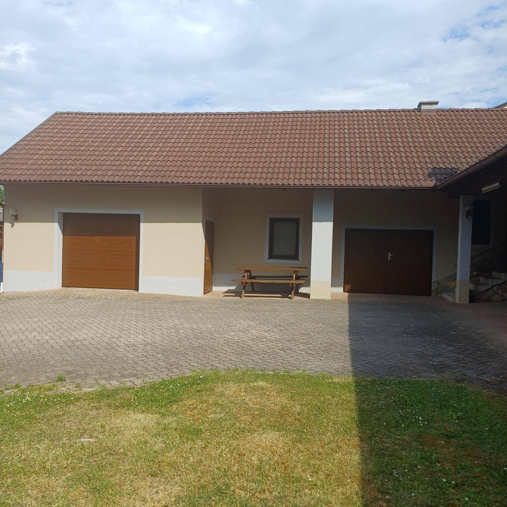Rückseite des Hauses mit zwei Garagentoren und einem großen gepflasterten Hofbereich, umgeben von Rasen.