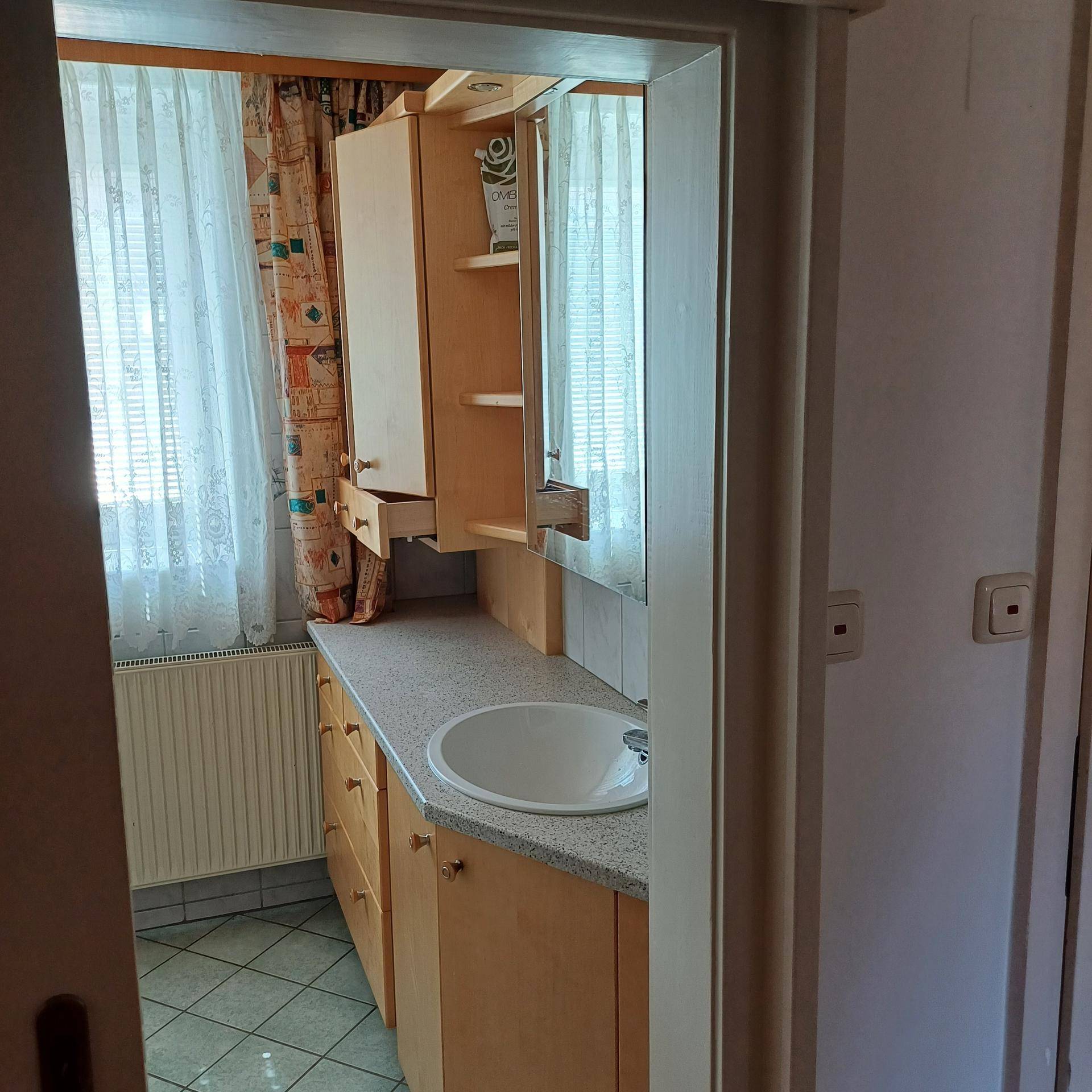 Helles Badezimmer mit Einzelwaschbecken, Spiegelschrank und Fenster, ausgestattet mit Fliesenboden.