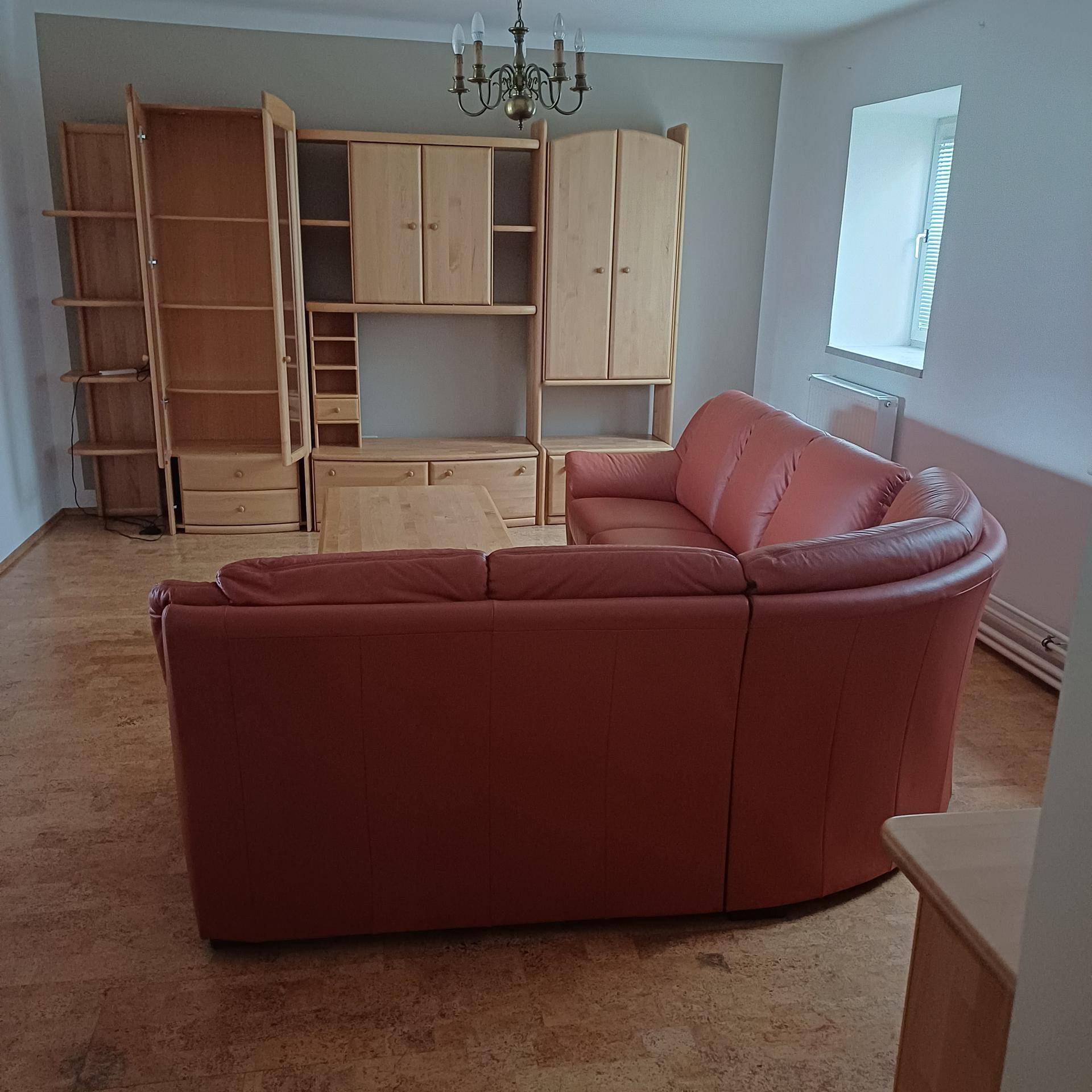 Geräumiges Wohnzimmer mit großer Ledercouch, Holzmöbeln und Korkboden, bereit zur individuellen Gestaltung.