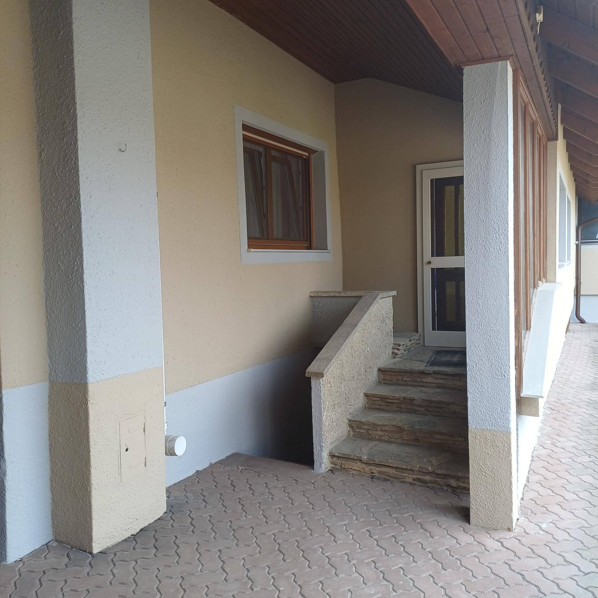 Überdachter Eingangsbereich mit Steinstufen und einer Haustür, umgeben von beigen Säulen und Wänden.