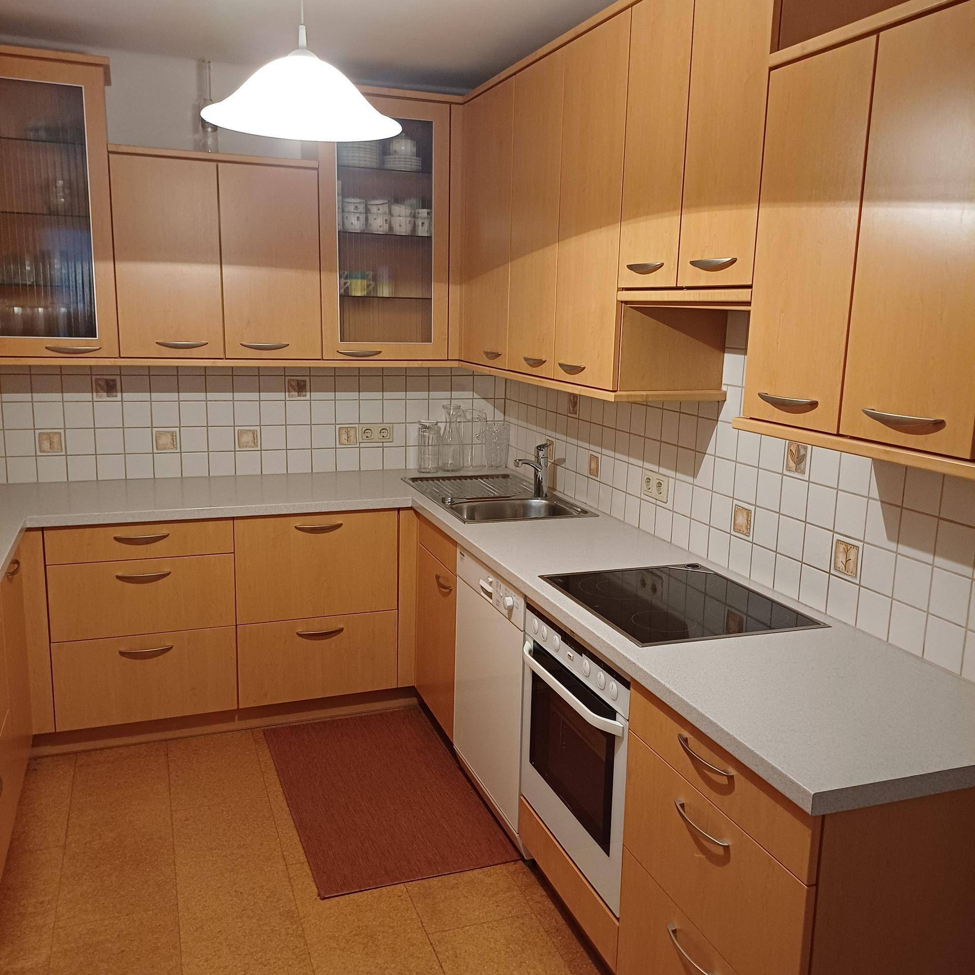 Funktionale Küche mit hellen Holzfronten, Induktionskochfeld, Backofen und Spülmaschine.