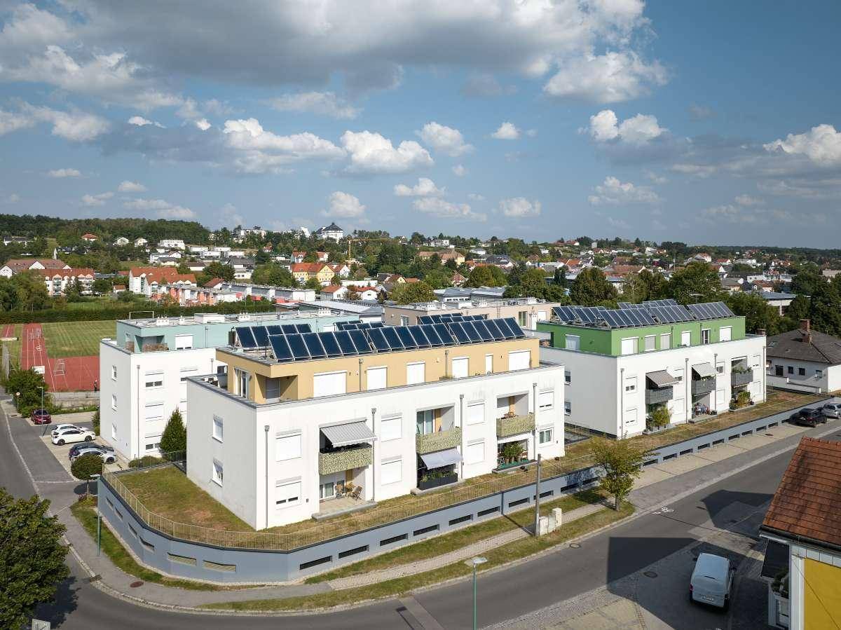 Mehrere moderne Wohngebäude mit Flachdächern, Balkonen und Solaranlagen unter blauem Himmel.