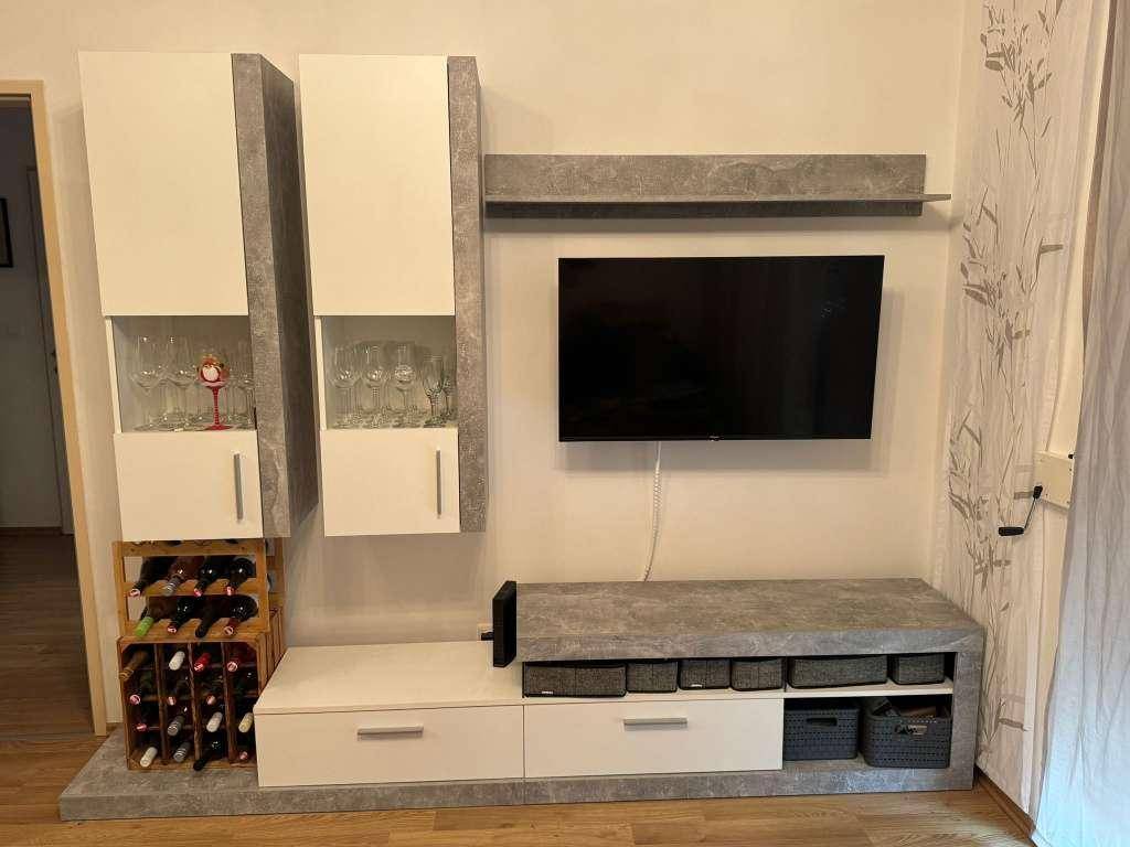 Wohnzimmer mit modernem TV-Möbel, Stauraum und Weinregal auf Holzboden.