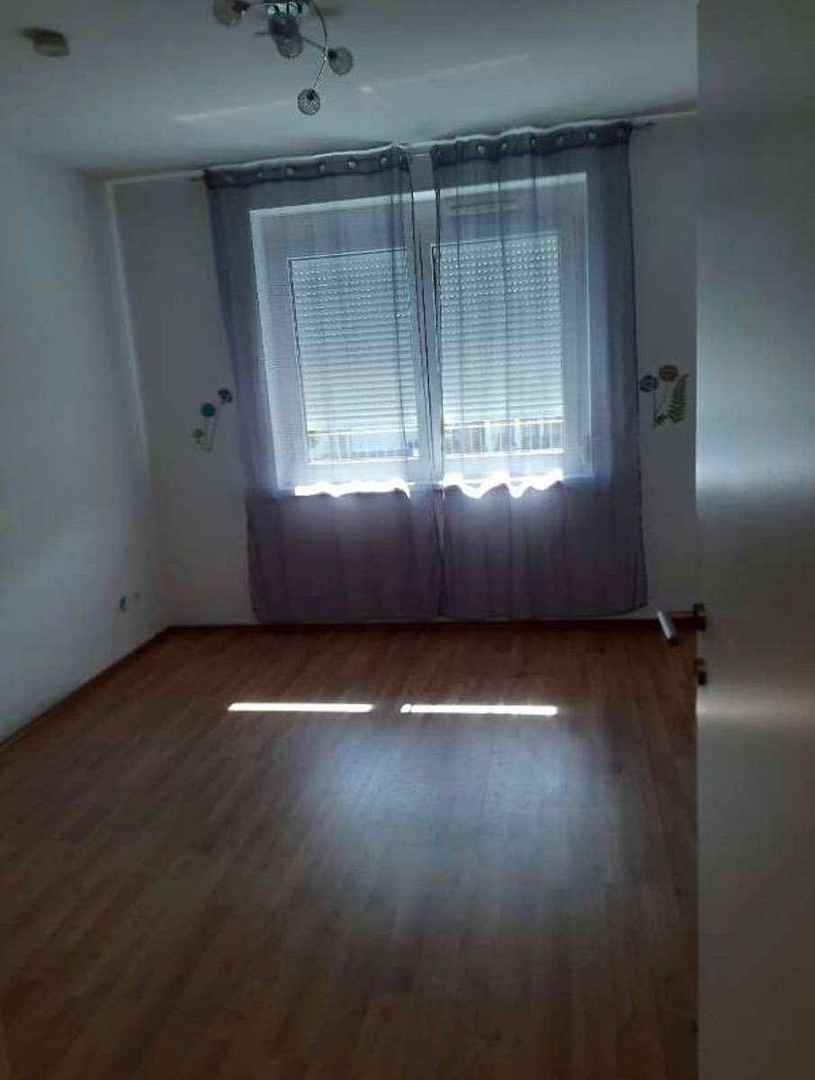 Leeres Schlafzimmer mit Holzboden und großem Fenster, das viel Tageslicht hereinlässt.