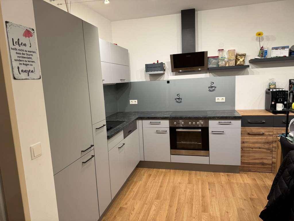 Funktionale Küche mit grauen Schränken, Holzboden und Dunstabzugshaube über dem Herd.