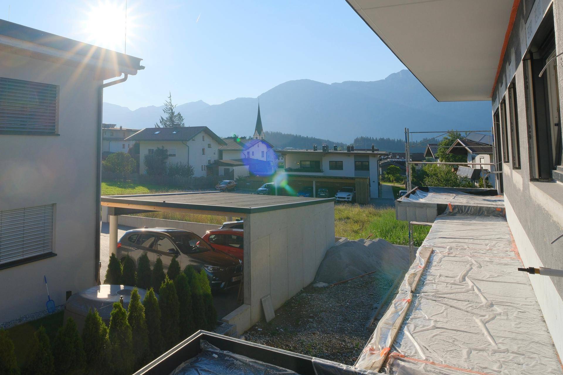 Blick von der Baustelle auf die umliegende Berglandschaft und benachbarte Häuser mit Carport.