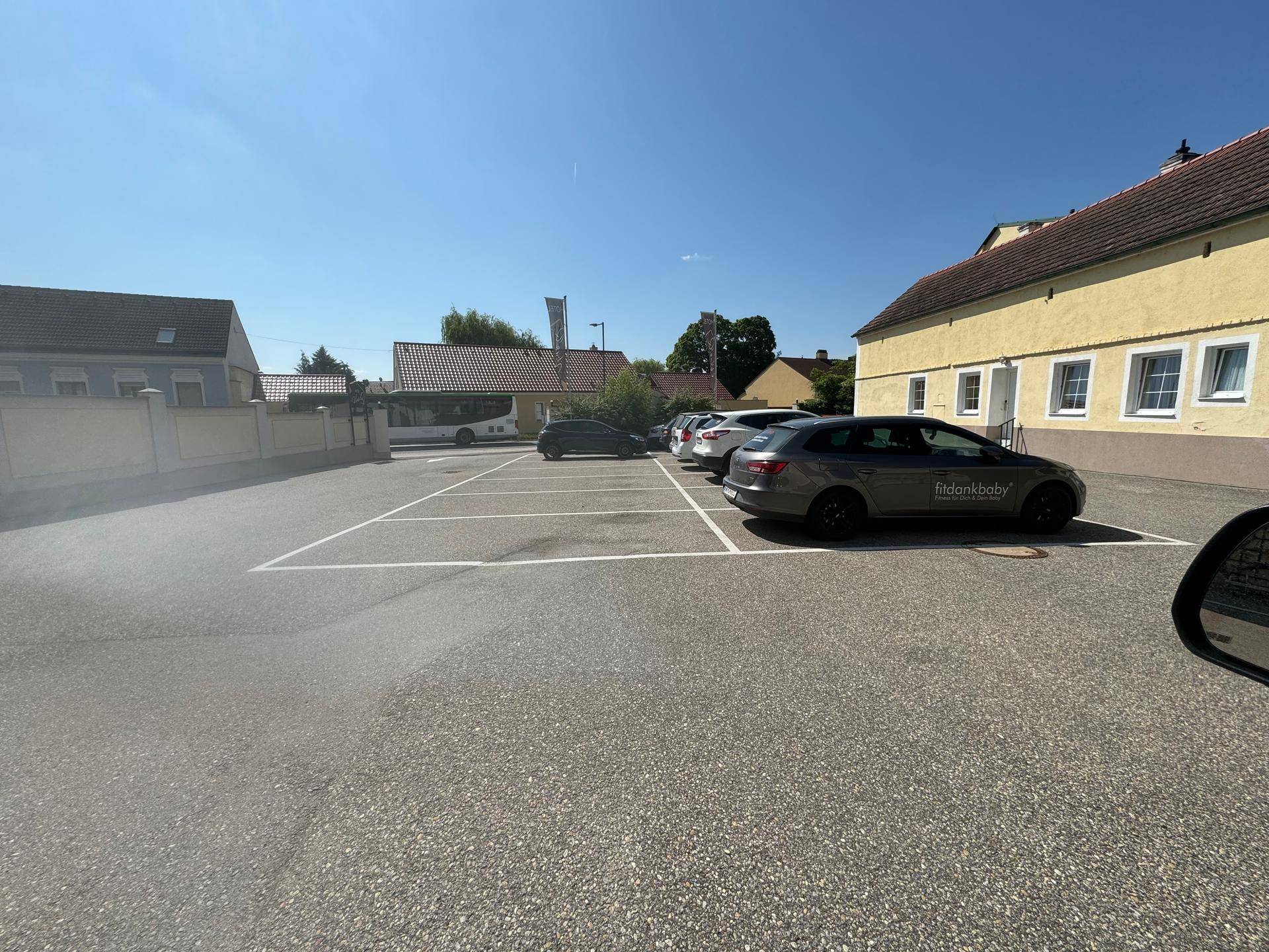 Außenansicht eines Parkplatzes mit mehreren Fahrzeugen und umliegenden Gebäuden unter blauem Himmel.