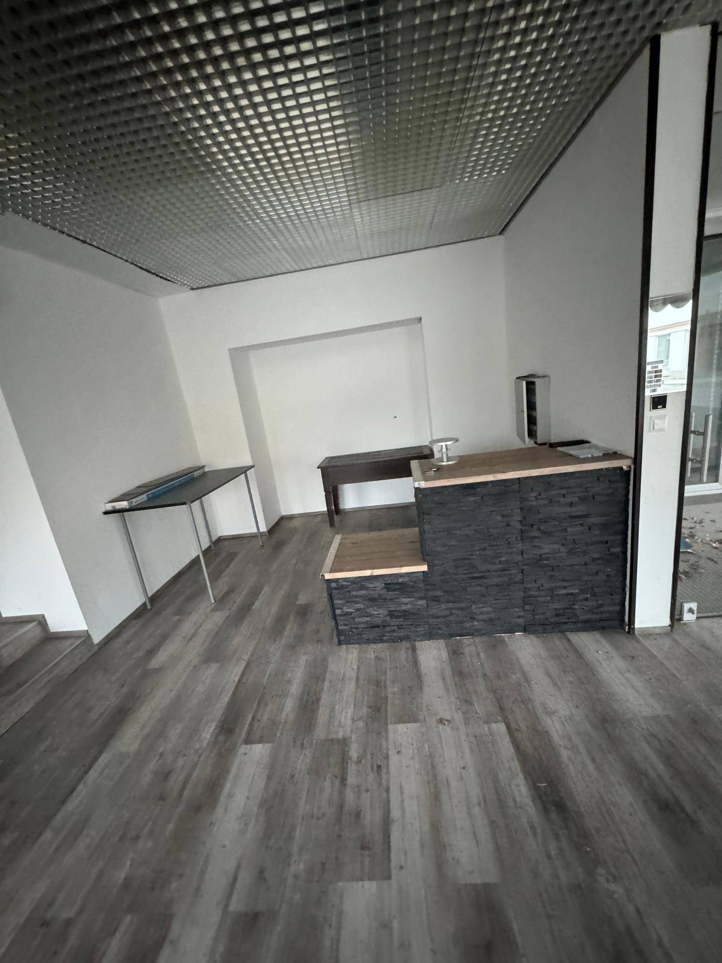 Heller Verkaufsraum mit Vinylboden, einer Theke und einer Nische im Hintergrund für Präsentationen.