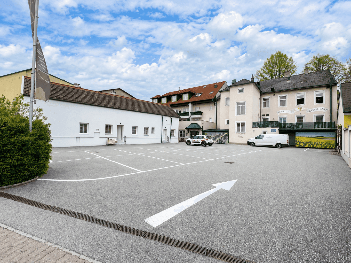 Großer Außenparkplatz mit markierten Stellplätzen und Gebäuden im Hintergrund unter blauem Himmel.