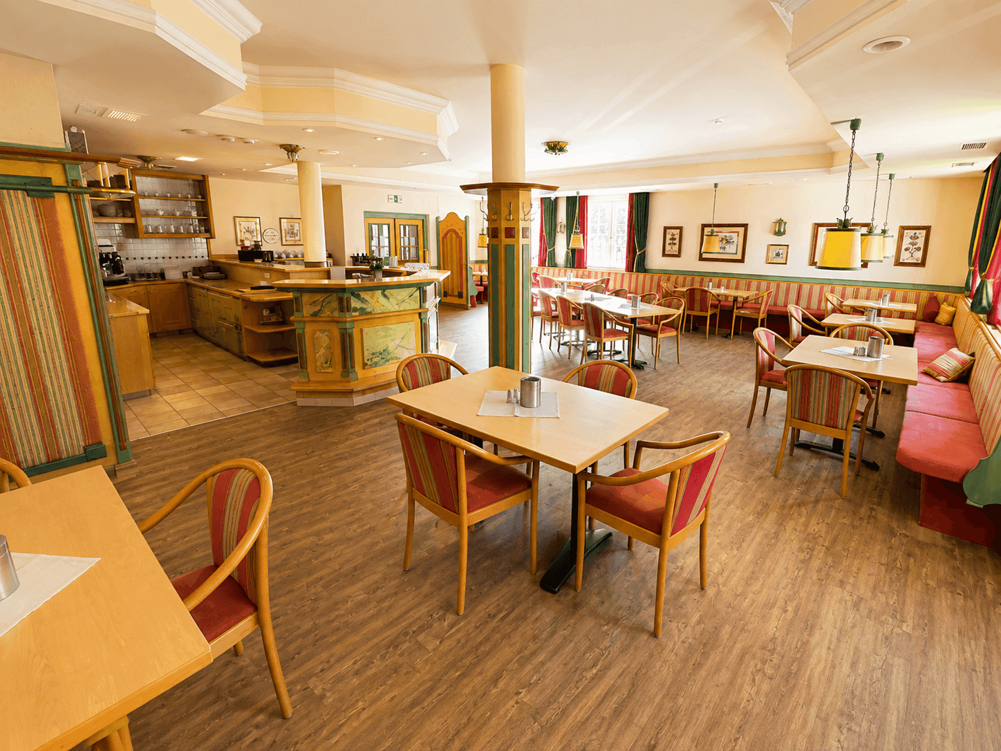 Heller Speisesaal mit Holzboden, traditionellen Möbeln und einem Barbereich im Hintergrund.