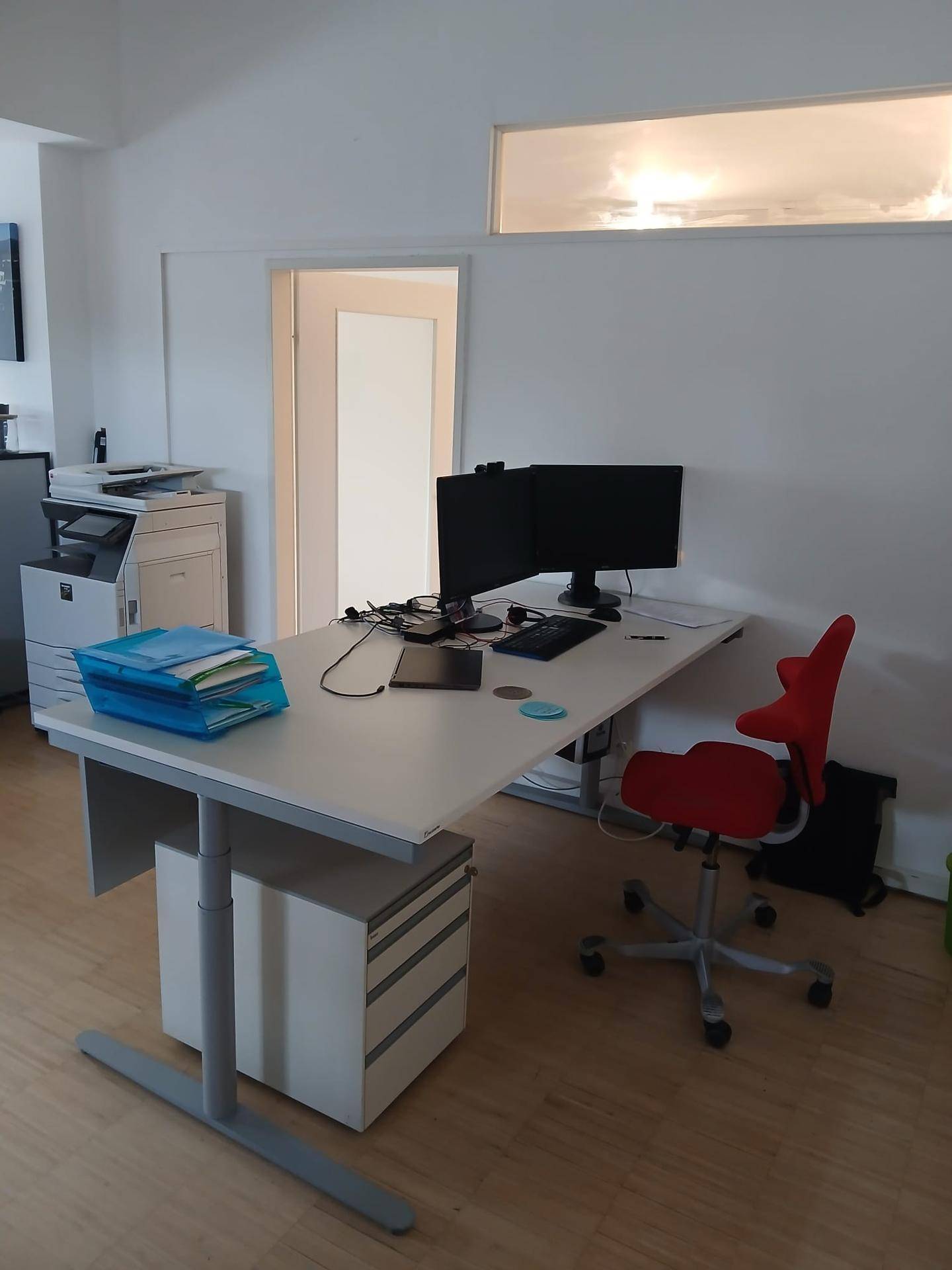 Moderner Büroschreibtisch mit Computer und ergonomischem Stuhl, beleuchtet durch ein Oberlichtfenster.