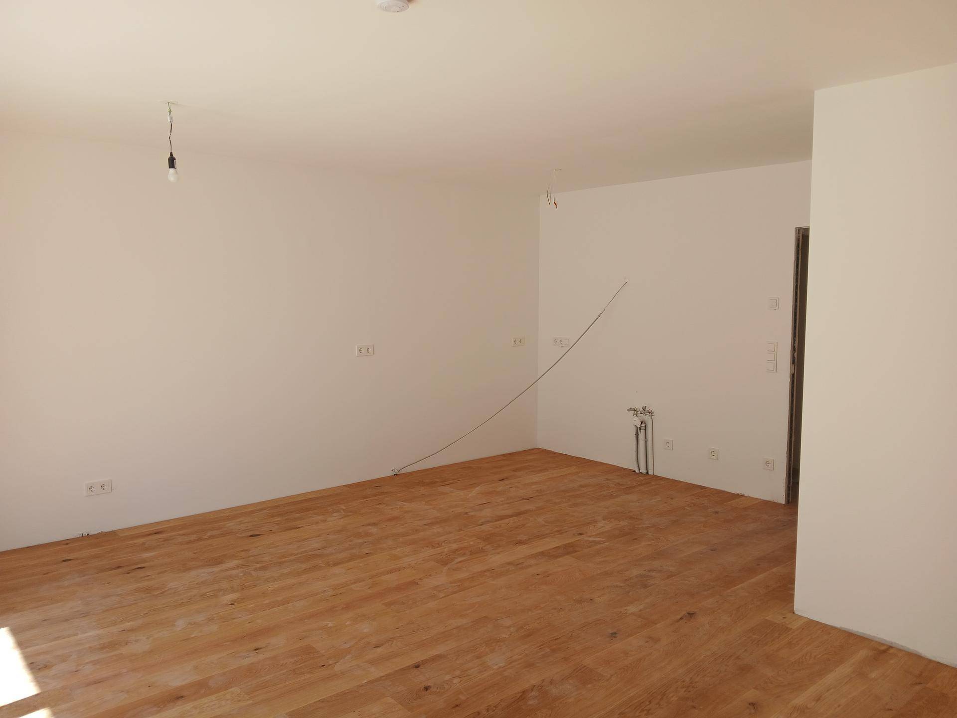 Heller, unmöblierter Raum mit neuem Holzfußboden und weißen Wänden, bereit für den Ausbau.