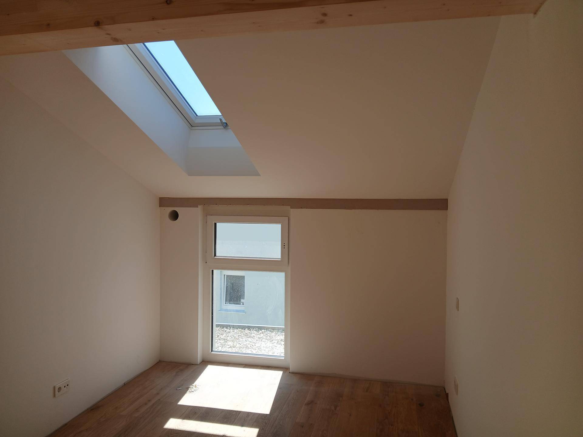 Lichtdurchfluteter Raum im Dachgeschoss mit Holzboden, Dachschräge und großem Dachfenster.