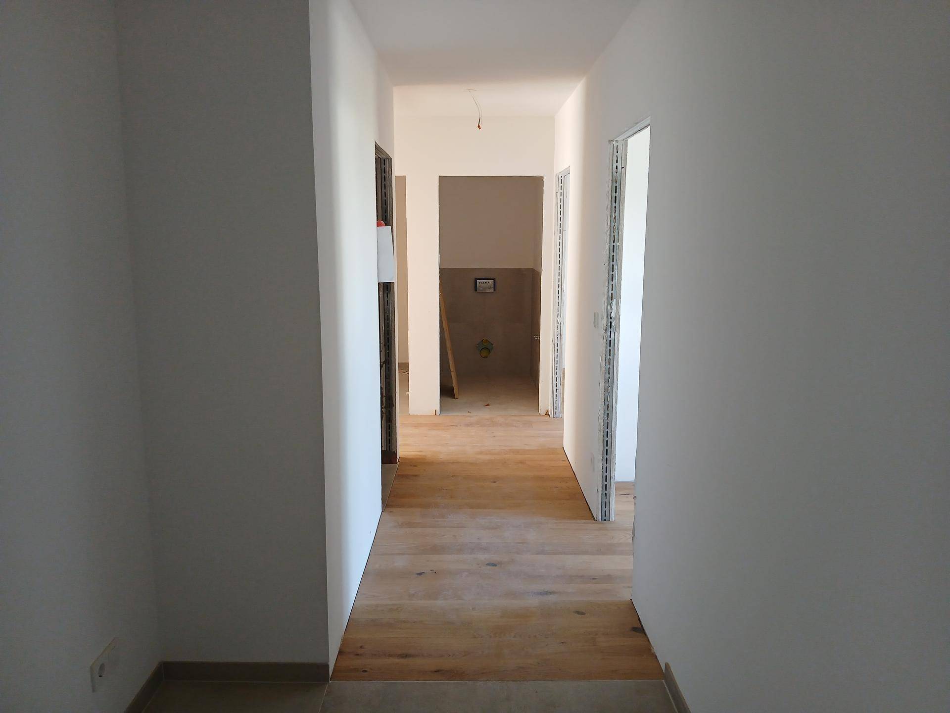 Langer, heller Flur mit Holzboden und mehreren Türöffnungen zu weiteren Räumen.