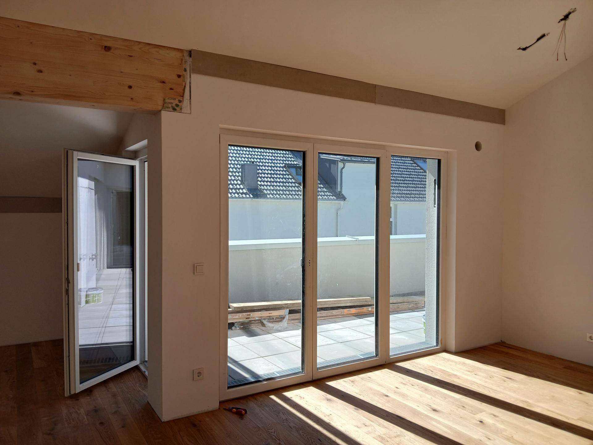 Lichtdurchfluteter Wohnbereich mit großen Glasschiebetüren, Holzboden und Zugang zu einer Terrasse.