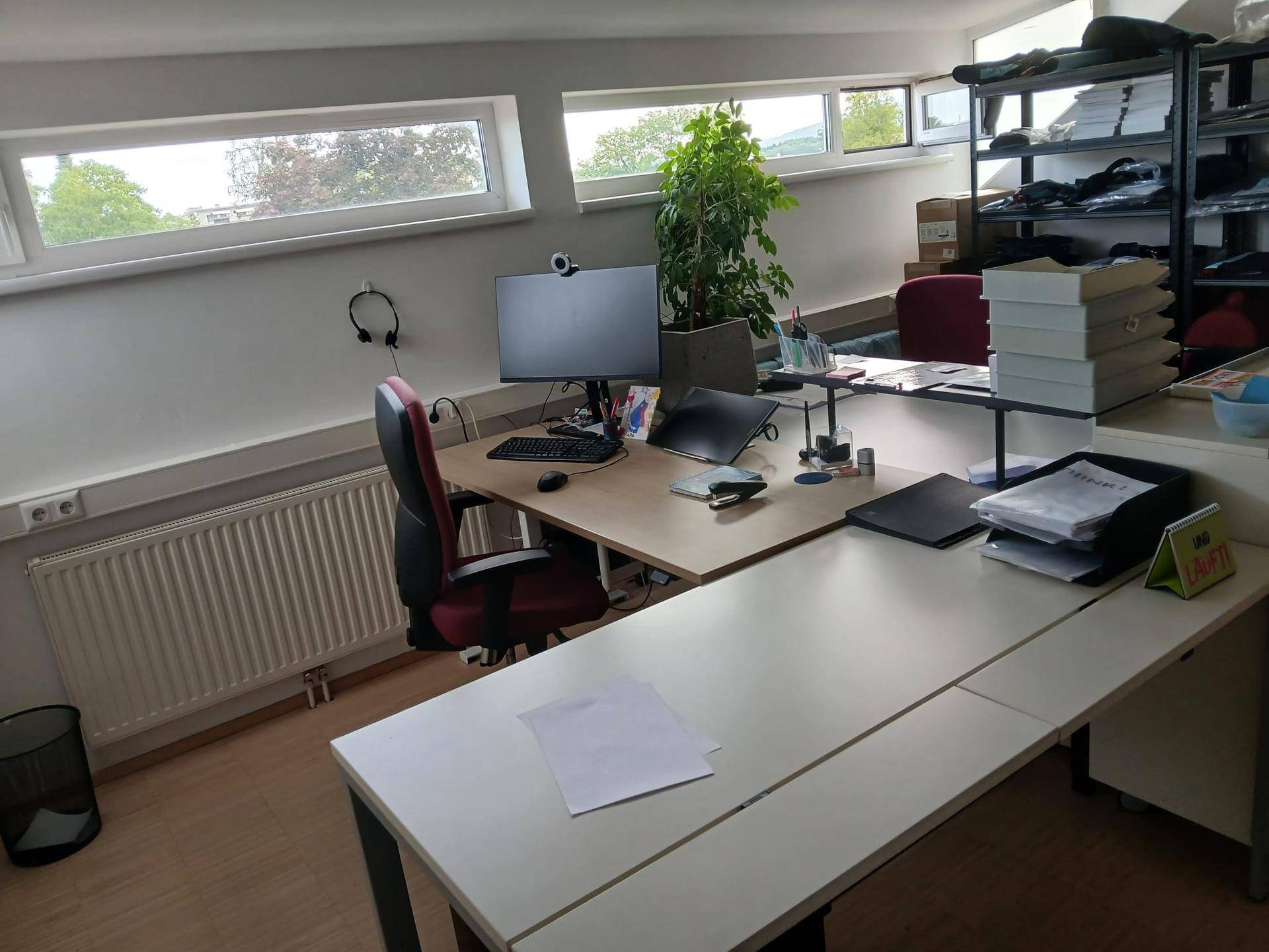 Weiterer Blick in das offene Büro mit Arbeitsplätzen, Heizkörper und Fenstern mit Blick ins Grüne.