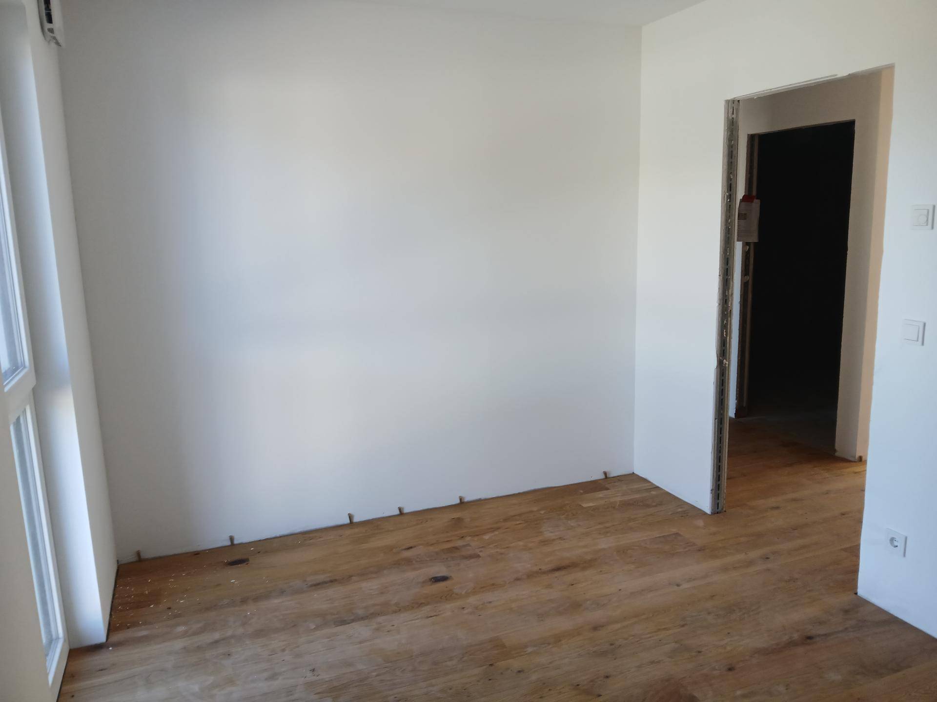 Lichtdurchfluteter Raum mit Holzboden und großem Fenster, bereit für die Einrichtung.