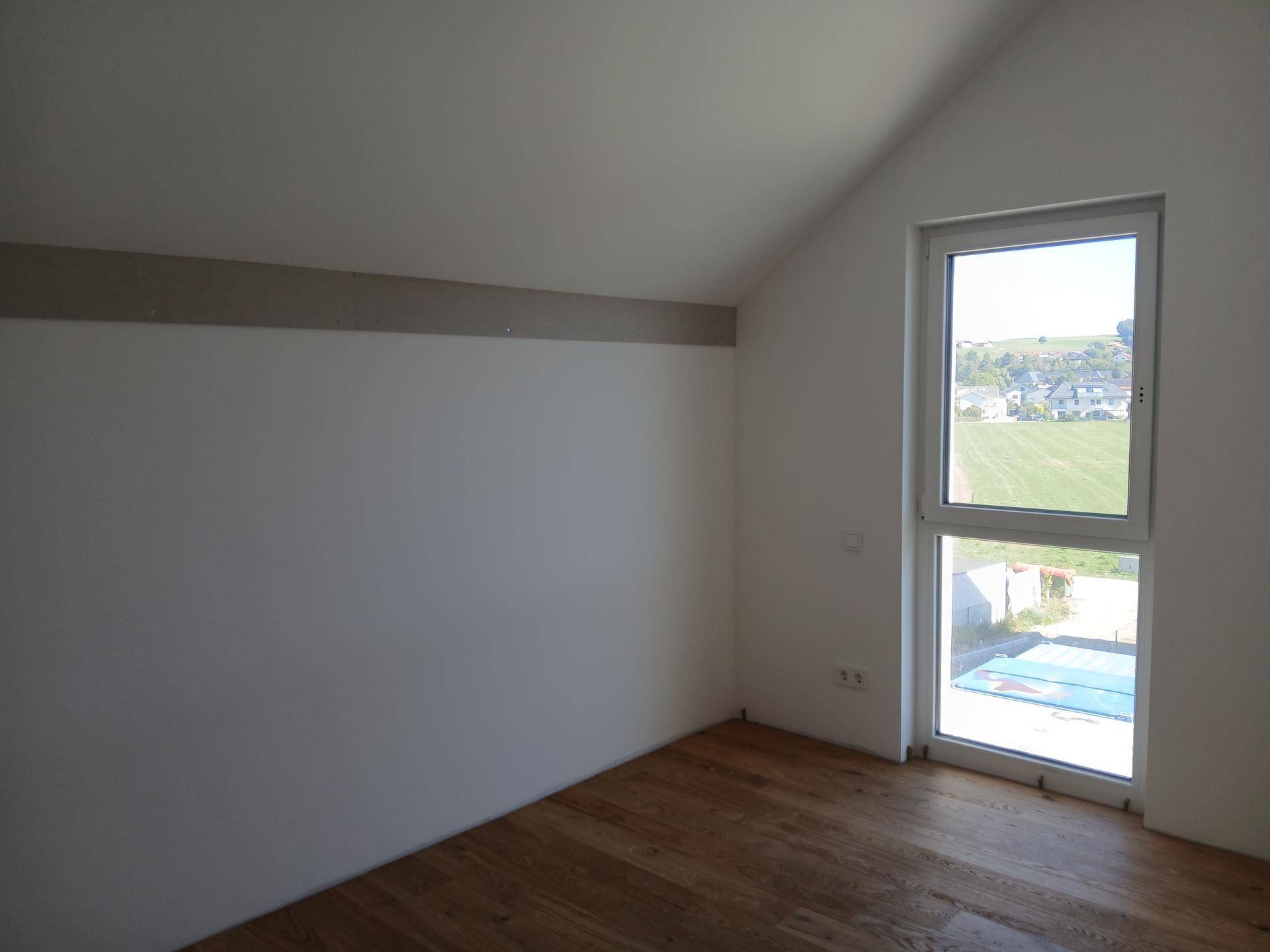 Helles Zimmer mit Holzboden, Dachschräge und weitem Blick ins Grüne und die umliegende Landschaft.