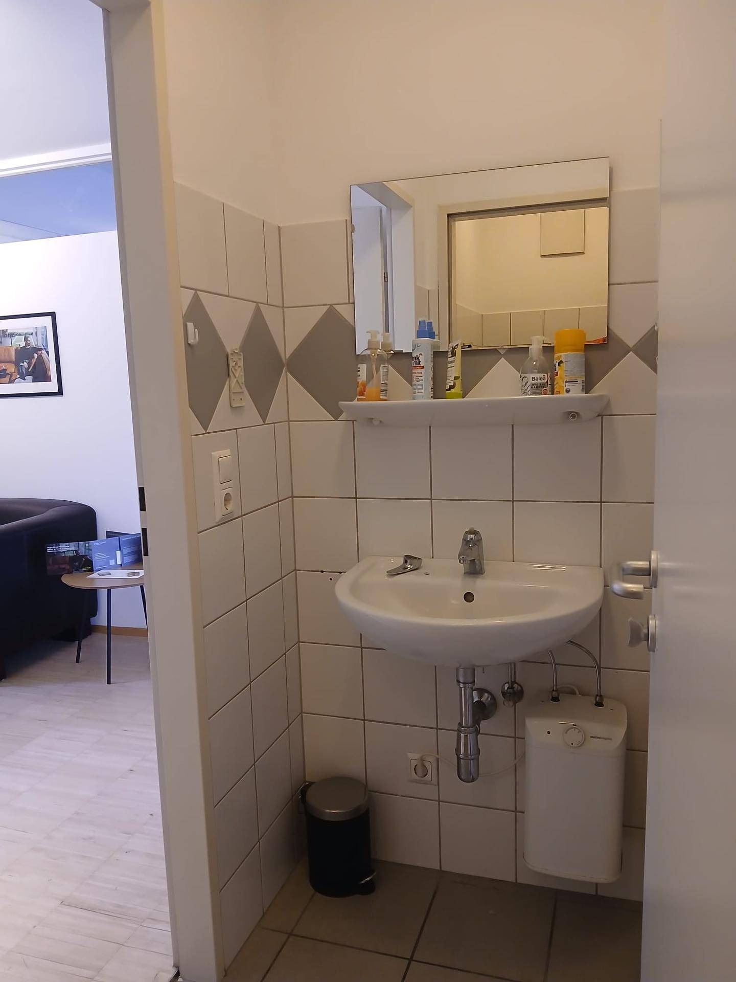 Kleines Badezimmer mit Waschbecken, Spiegel und gefliesten Wänden in weiß und grau.