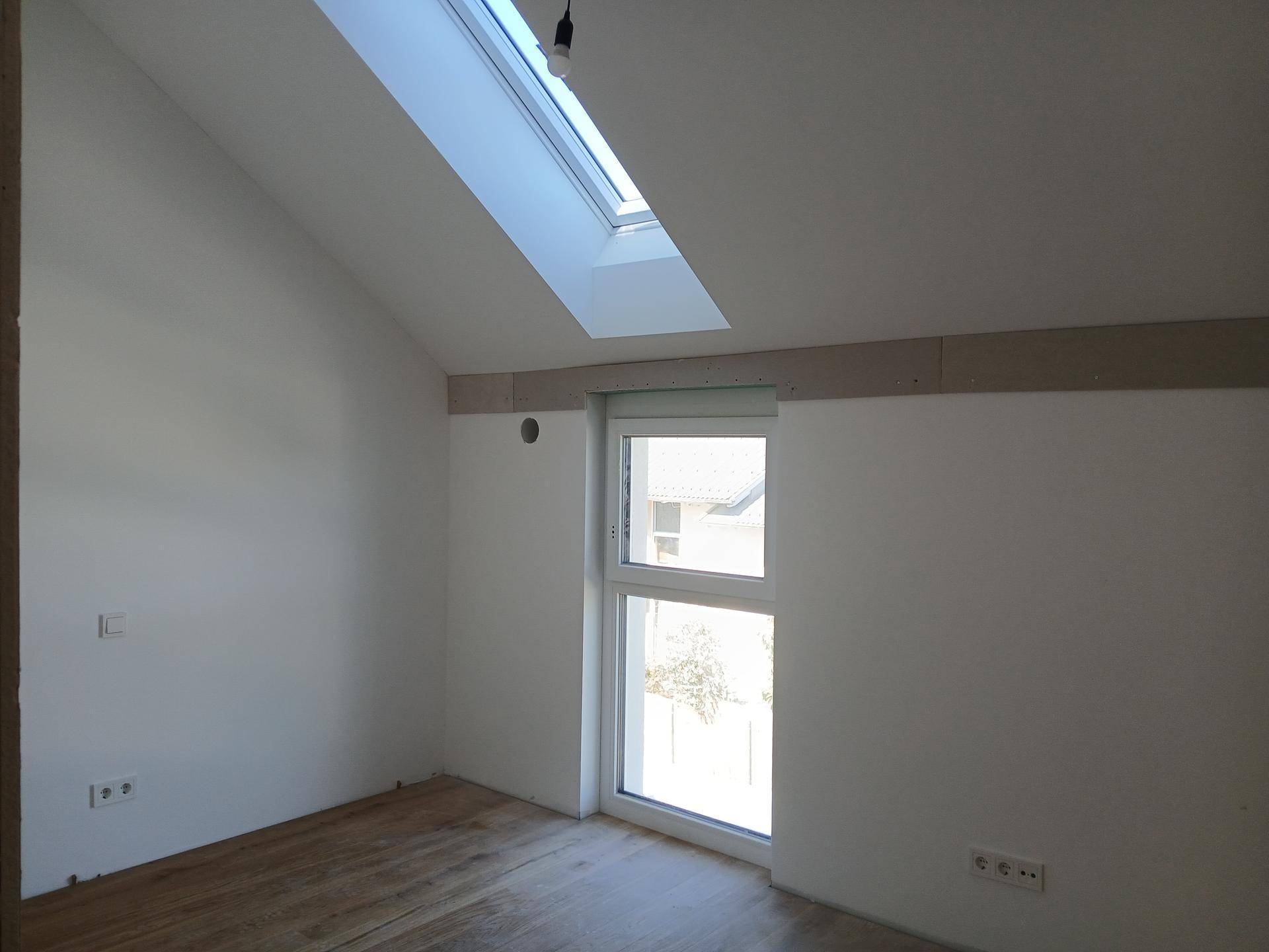 Helles Schlafzimmer mit Dachschräge, Holzboden und Dachfenster für viel Tageslicht.