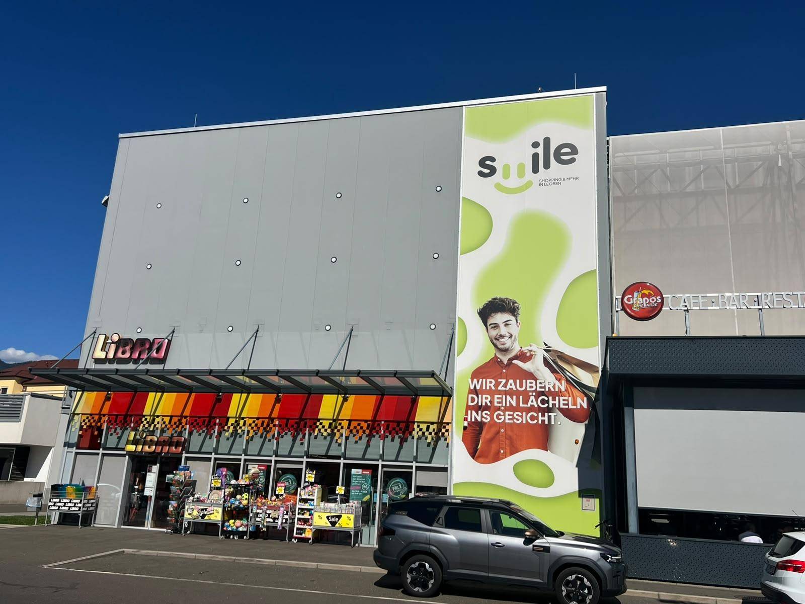 Fassade eines Geschäftsgebäudes mit dem Libro-Logo und einer Werbetafel, umgeben von einem Parkbereich.