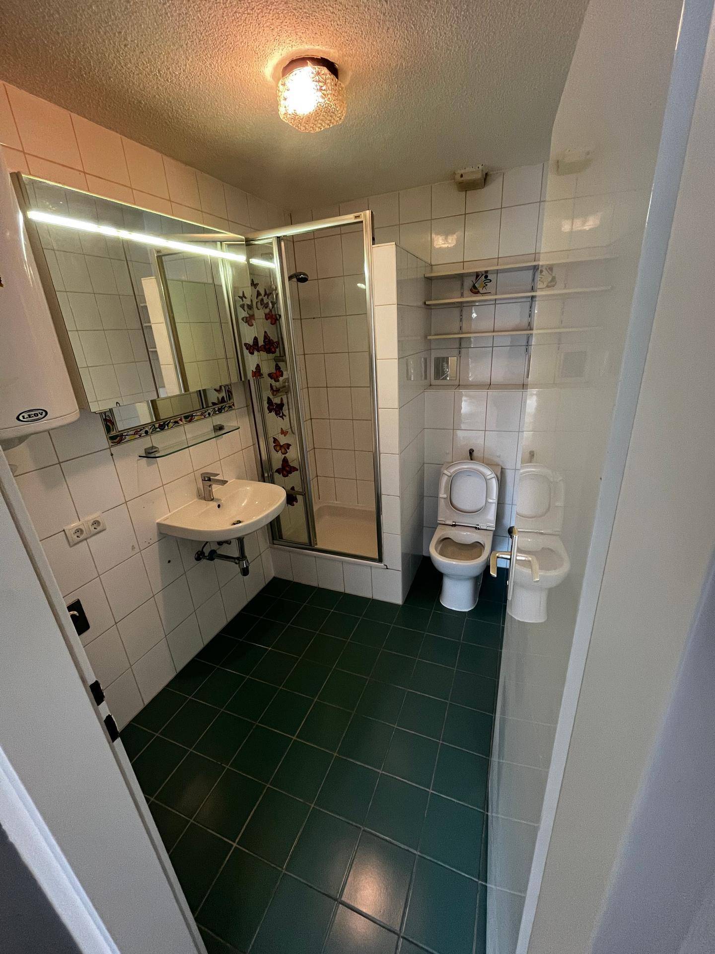 Badezimmer mit weißen Wandfliesen, dunkelgrünem Boden und Duschkabine.