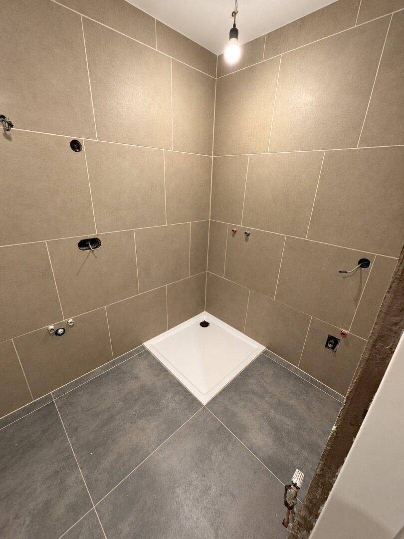 Modern gefliestes Badezimmer mit Duschbereich und Vorbereitung für Armaturen.
