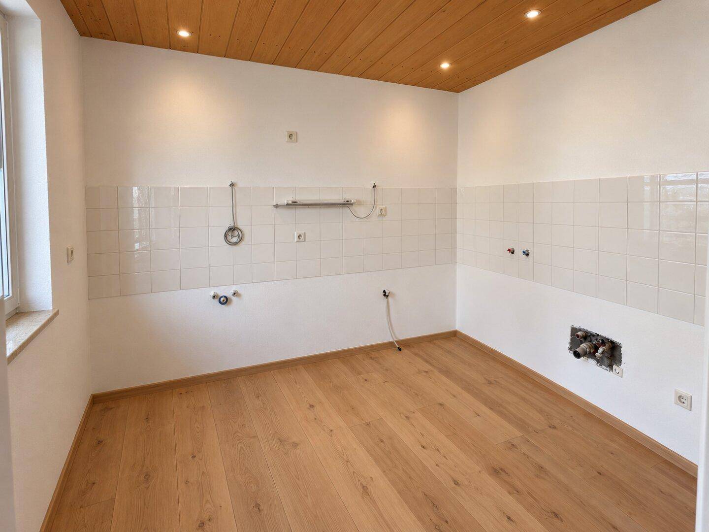 Leere Küche mit Holzboden, weißen Fliesen und Holzdecke, bereit für den Einbau.