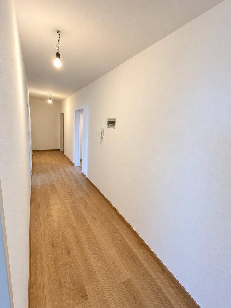 Langer, heller Flur mit Holzboden und weißen Wänden, der zu weiteren Räumen führt.