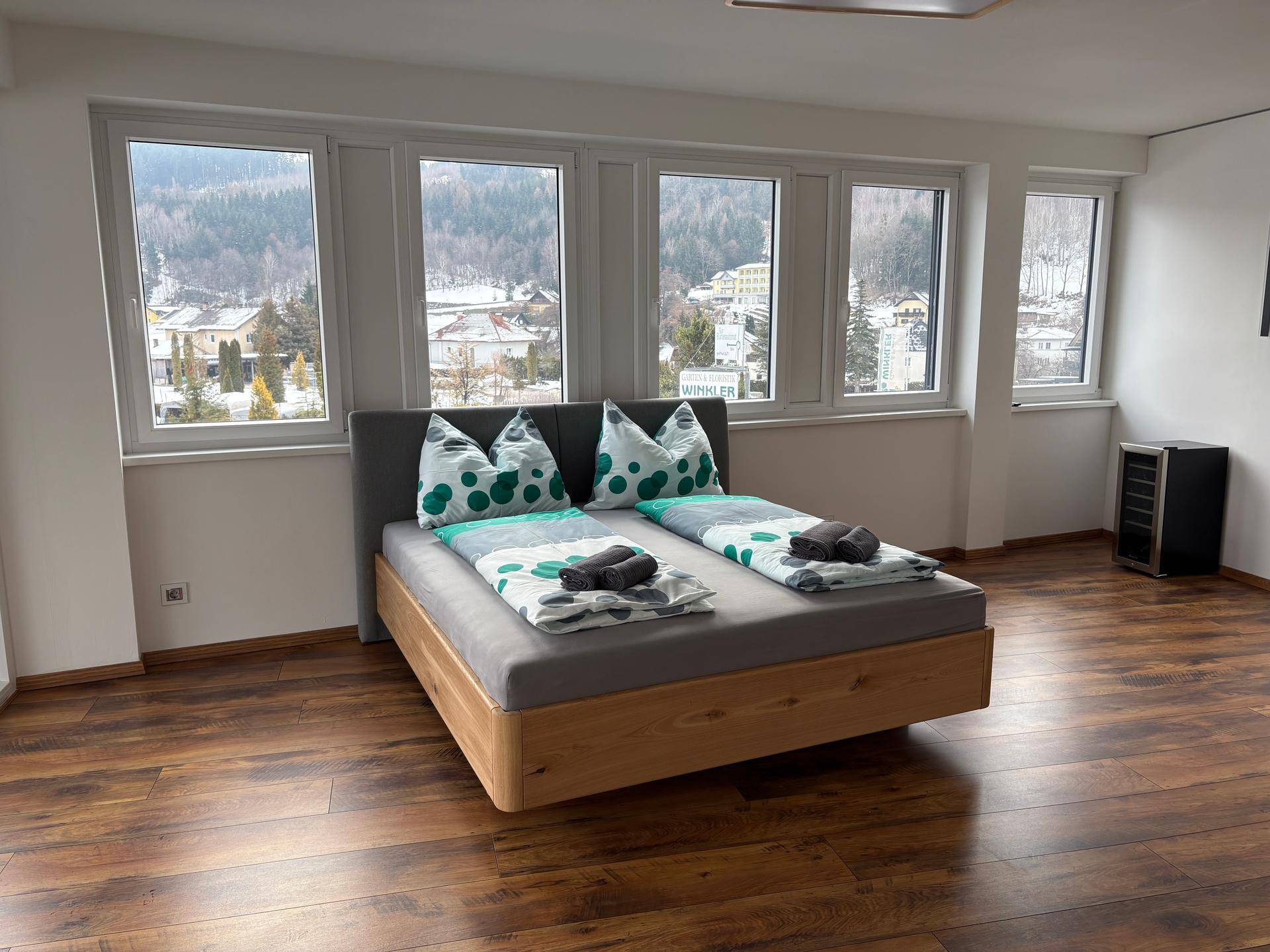 Gemütliches Schlafzimmer mit Holzboden und weitem Blick auf die umliegende Berglandschaft durch große Fenster.