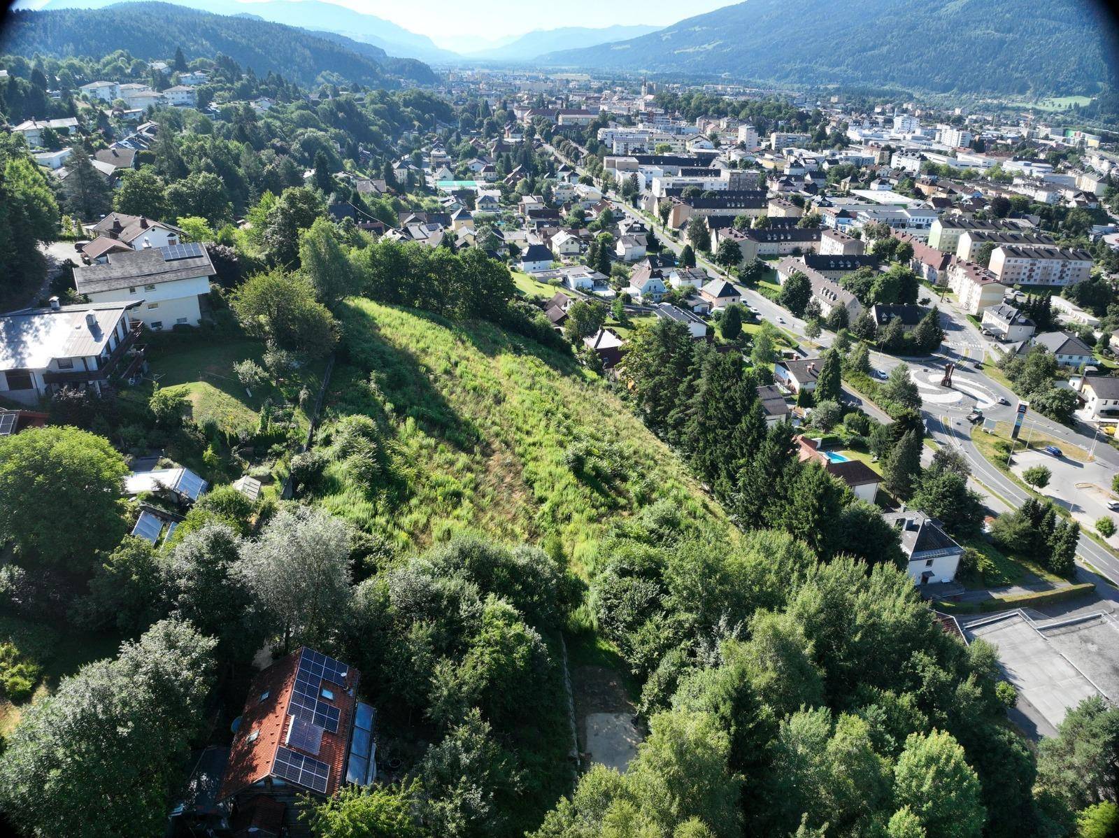 Luftaufnahme eines Baugrundstücks mit umliegender Wohnbebauung und Blick auf die Stadt.
