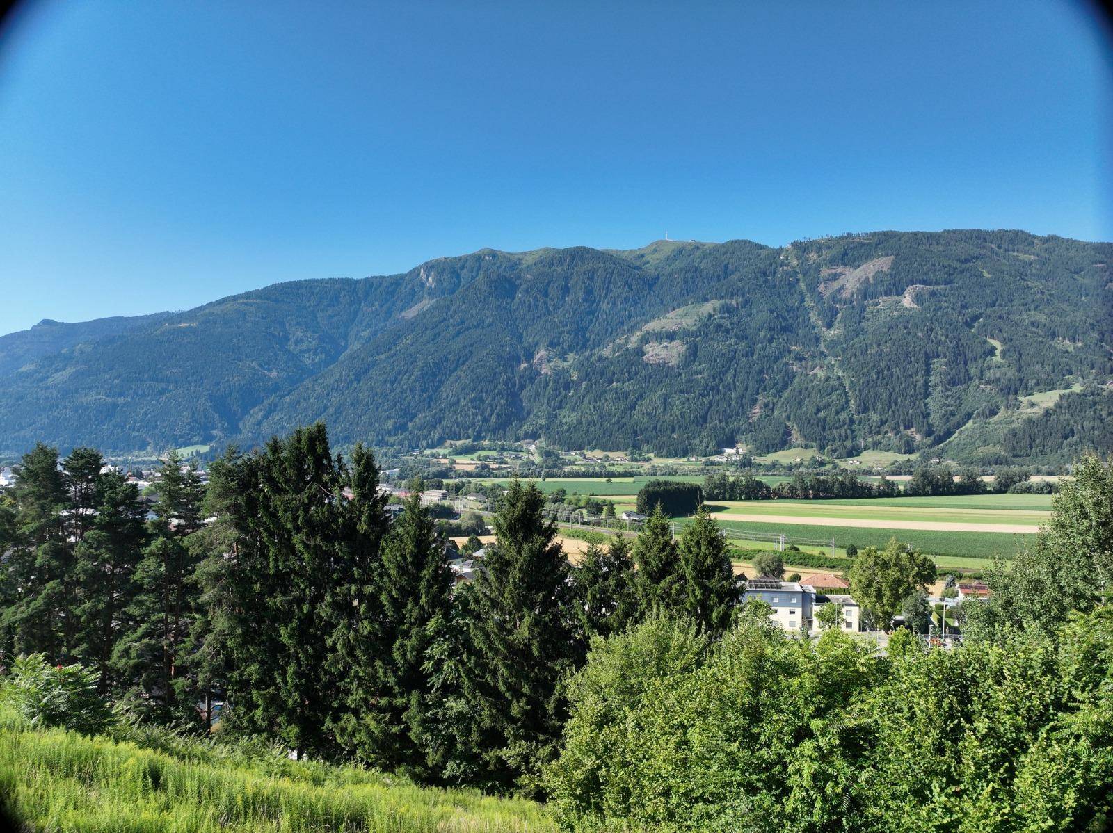 Panoramablick auf weite grüne Felder und majestätische Berge unter einem klaren blauen Himmel.