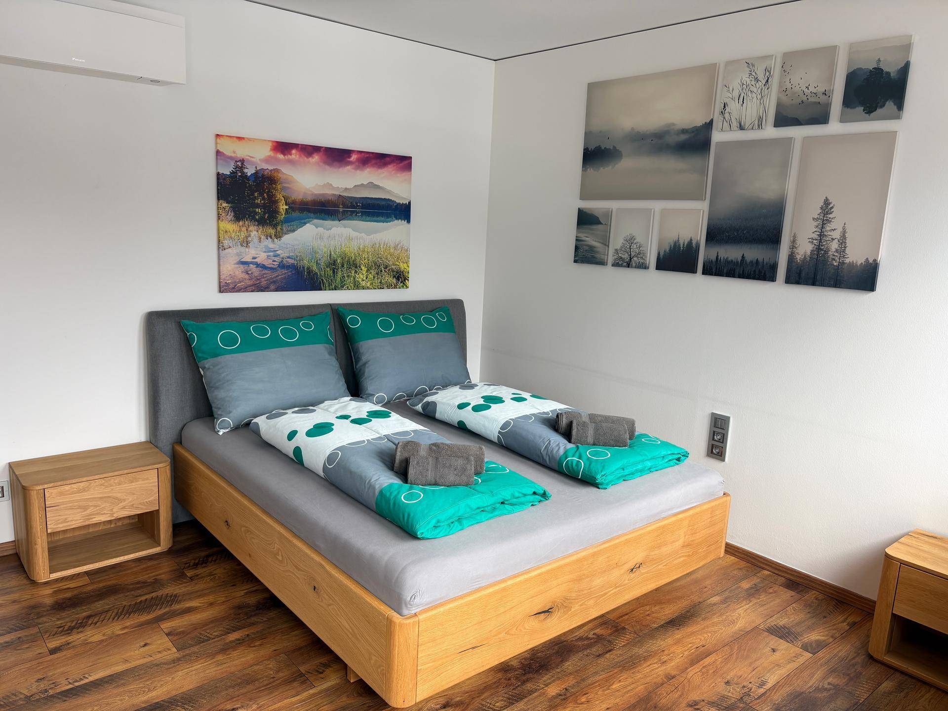 Modernes Schlafzimmer mit Holzbett, Nachttischen, Klimaanlage und farbenfrohen Landschaftsbildern an der Wand.