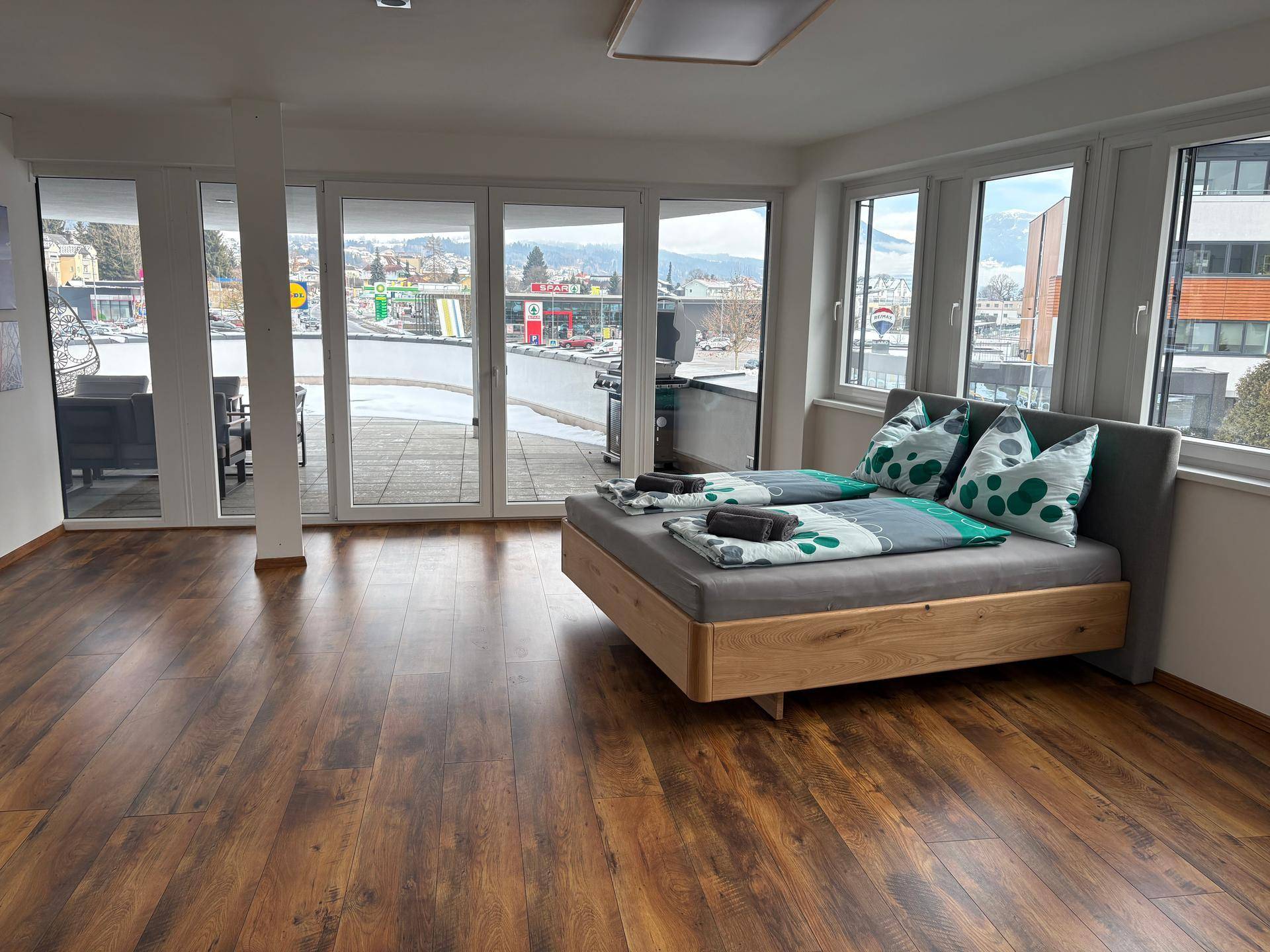 Helles Schlafzimmer mit Holzboden, modernem Bett und großen Fenstern mit Zugang zur Terrasse.