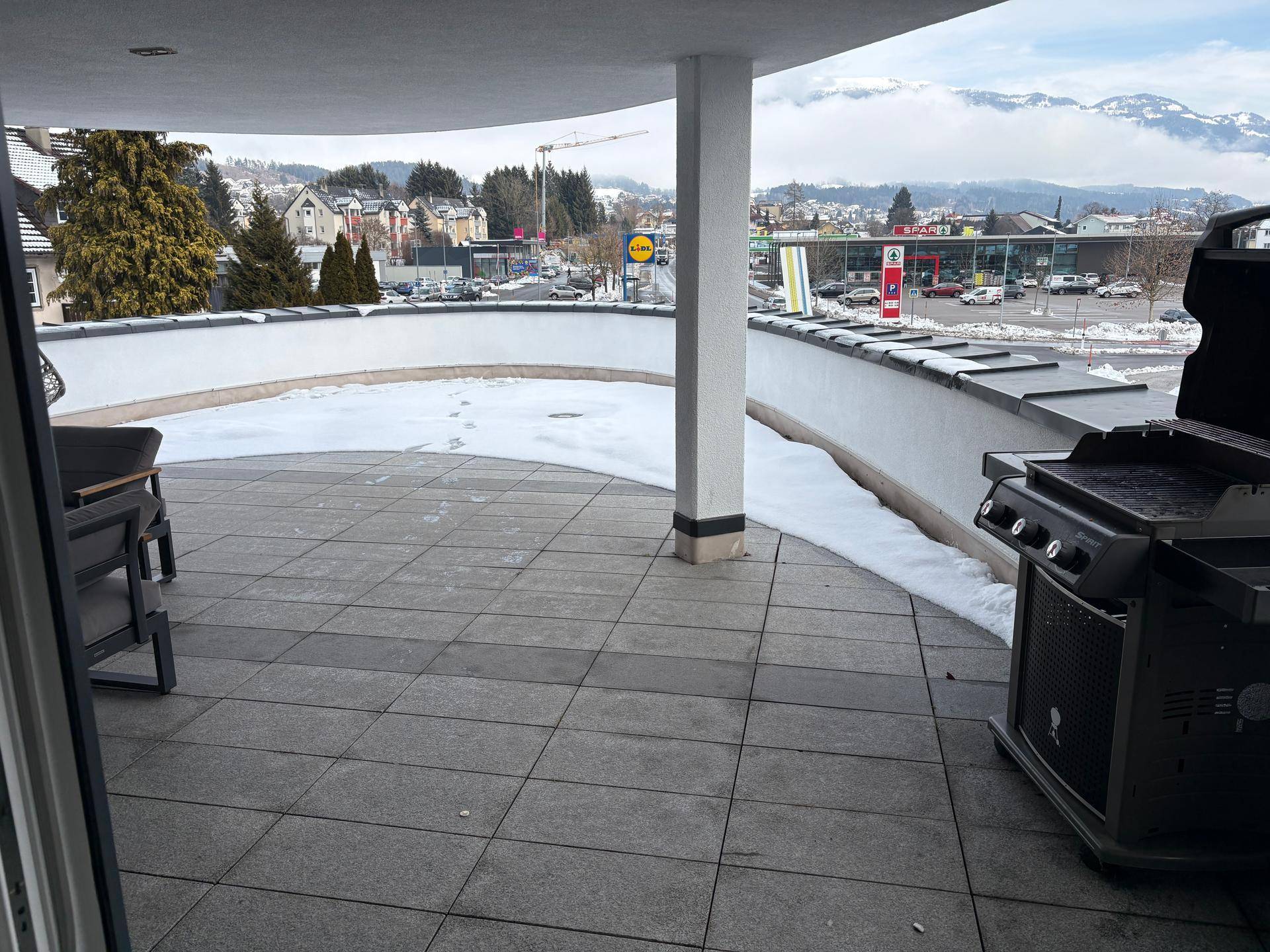 Überdachte Terrasse mit Grill und Blick auf die umliegende Stadtlandschaft, teilweise mit Schnee bedeckt.