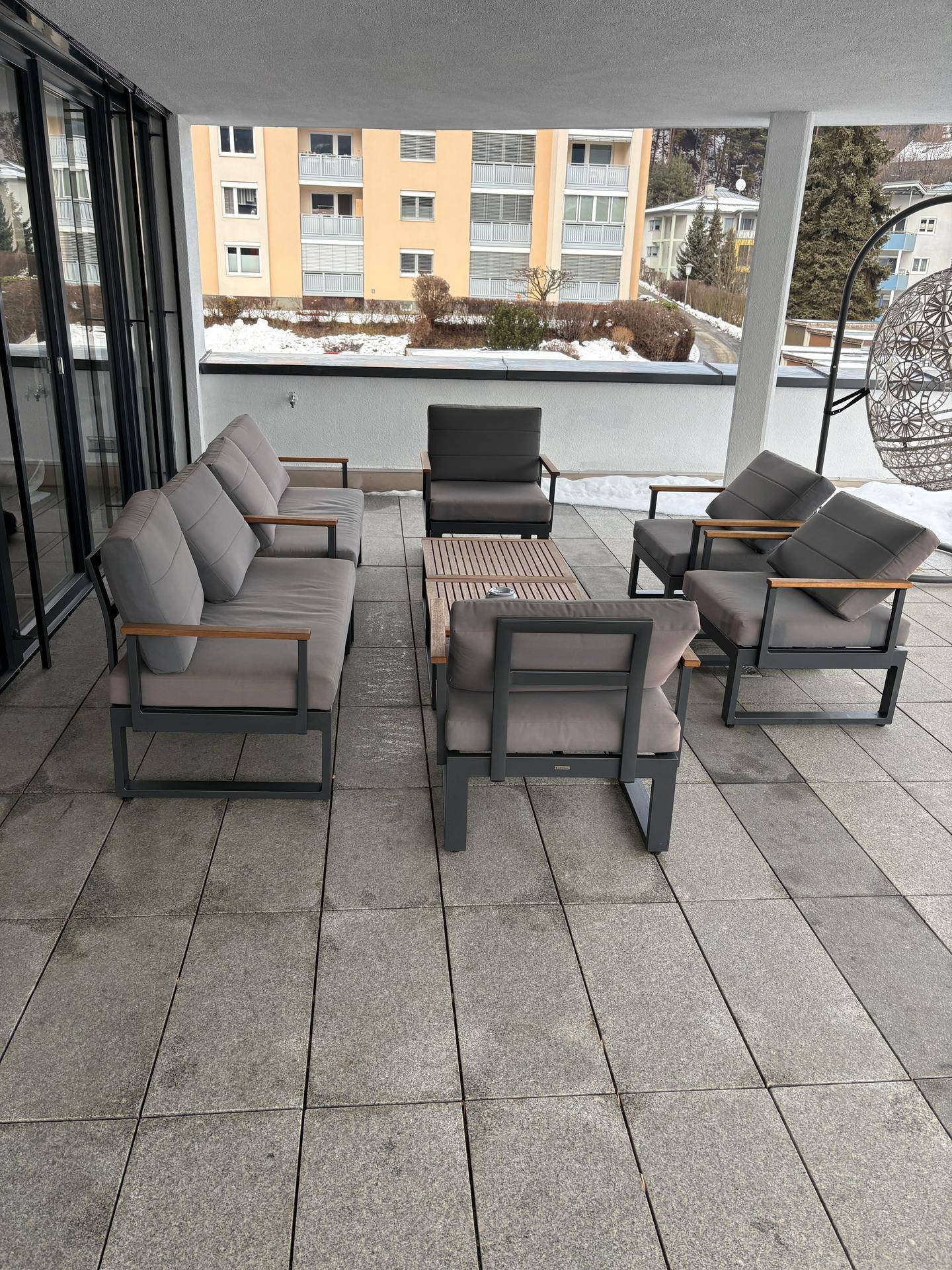 Geräumige Terrasse mit modernen Outdoor-Möbeln und Fliesenboden, umgeben von winterlicher Landschaft.