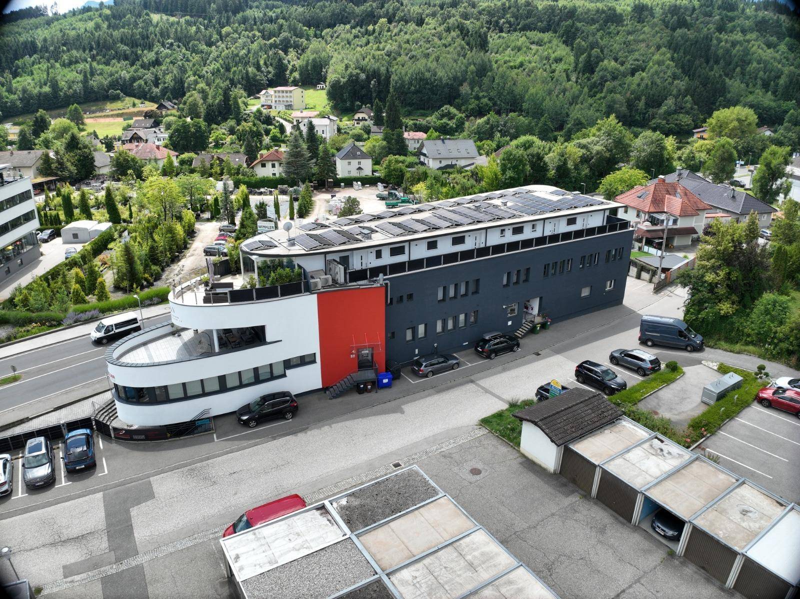 Luftaufnahme der Gewerbeimmobilie von der Seite, mit Solaranlage auf dem Dach und Parkplätzen.